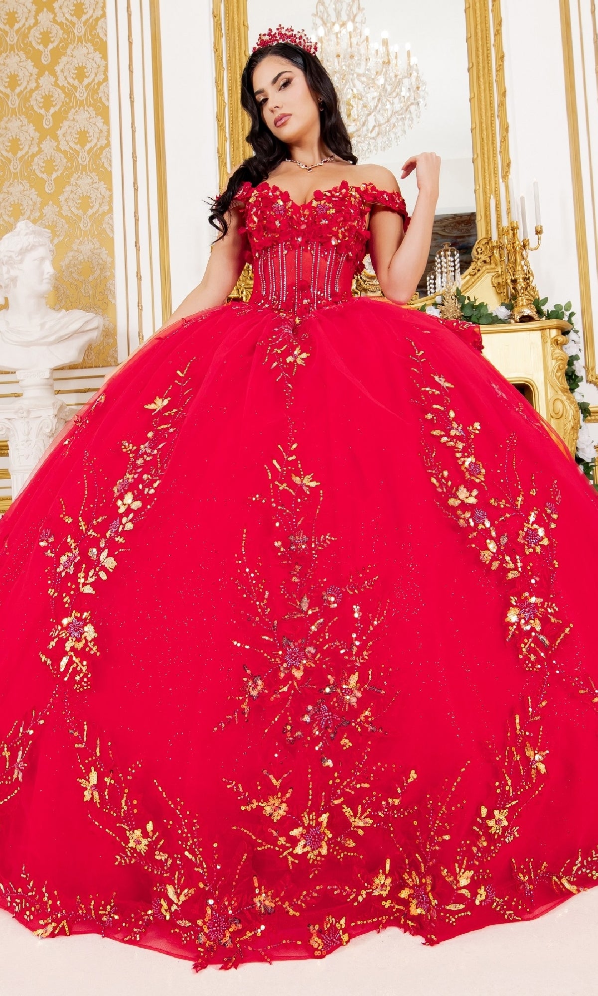 A woman models the Cinderella Couture 8160J quinceanera dress—a luxurious off-the-shoulder ball gown with gold floral embroidery and matching crown—posing indoors in an elegant, gold-accented room.